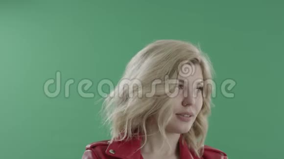 年轻的金发腼腆的迷人女子穿着红色夹克对着绿色的屏幕笑视频的预览图