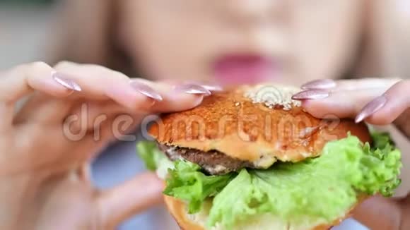一位饥饿的美丽女孩吃着美味的新鲜汉堡享受着快餐视频的预览图