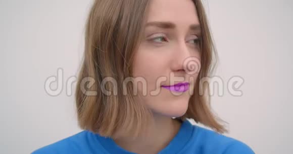 年轻的短头发女性的特写肖像涂着紫色口红看着白色背景的镜头视频的预览图
