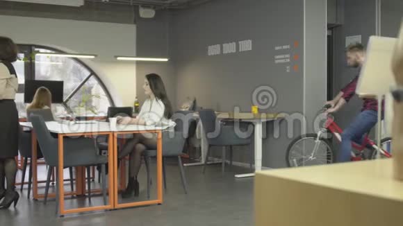 成熟的女人和她年轻时尚的同事在办公室交谈在背景中年轻人把自行车放在附近视频的预览图