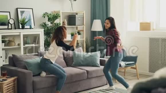 美丽的亚洲女孩穿着休闲服装时髦衬衫和牛仔裤在家跳舞而她的非裔美国朋友视频的预览图
