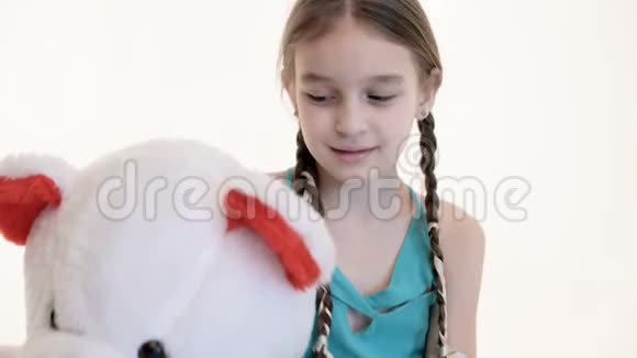一个可爱的白色女孩的肖像她扎着辫子抱着一只大泰迪熊坐在地板上背景是白色的视频的预览图