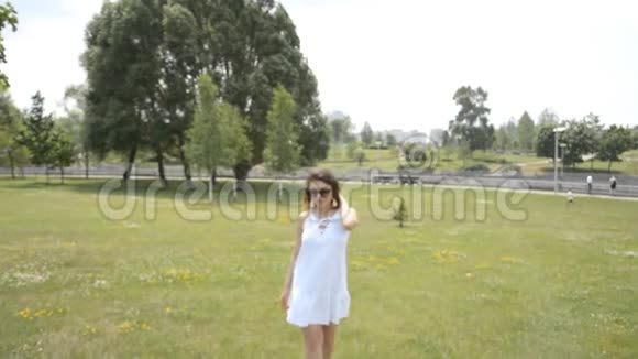 穿着白色夏装和卷发的漂亮女孩在夏季公园散步视频的预览图