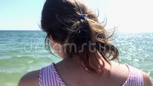 一位年轻的高加索女人站在海滩上双臂举在空中向外眺望大海视频的预览图