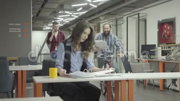 漂亮的女人坐在办公室的工作场所做她的工作一个满脸笑容的男人骑着他的自行车带着文件视频的预览图
