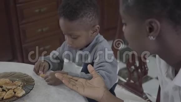 漂亮的非裔美国妇女和她的小儿子坐在桌子旁在盘子里放饼干的画像视频的预览图