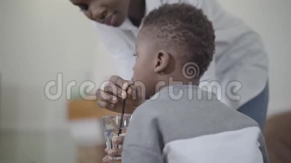 慈爱的母亲帮助非裔美国小男孩用管子从玻璃中喝水夫妻关系快乐视频的预览图