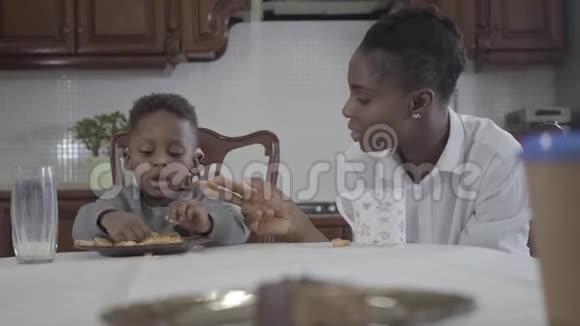 美国黑人妇女和她的小儿子坐在桌子旁在盘子里放饼干视频的预览图