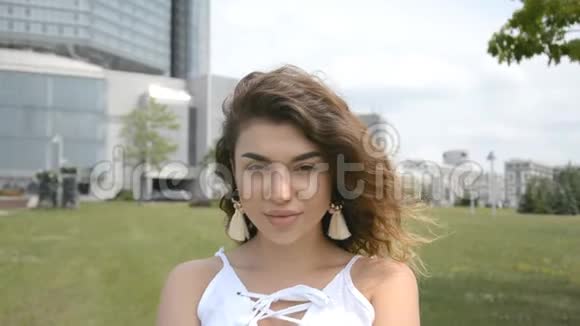 长着深色卷发的漂亮女孩在城市公园里看摄像机视频的预览图