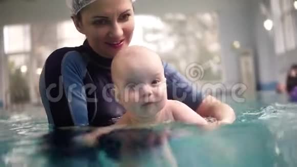 快乐的小男孩和他妈妈一起在游泳池里游泳她抱着他教他如何视频的预览图