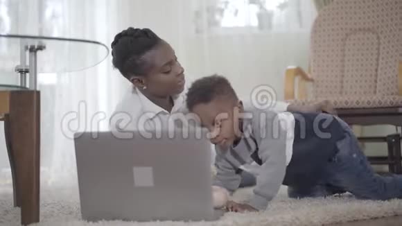 肖像快乐的非裔美国妇女和她可爱的儿子躺在地毯上在网上搜索一些东西视频的预览图