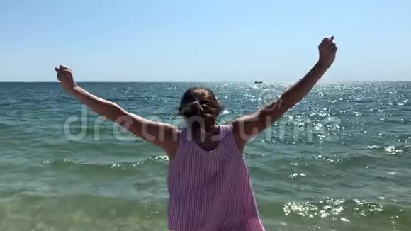 一位年轻的白种人女子站在海滩上双臂举在空中眺望大海她的侧观察视频的预览图