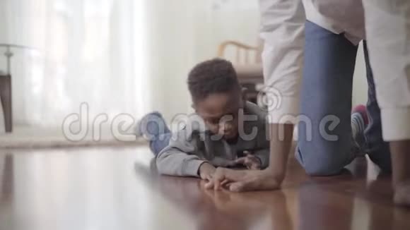 这个男孩在地板上爬行他的母亲就在附近非裔美国人的母亲和小儿子在家过一个愉快的周末视频的预览图