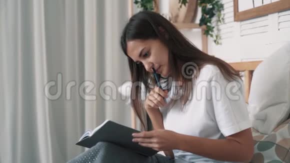 漂亮的女人坐在床上在日常计划中做笔记慢动作视频的预览图