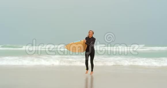 积极的非裔美国女性冲浪者冲浪板在海滩上奔跑的正面景色视频的预览图
