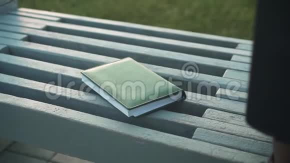 一本笔记本放在长凳上的特写女手拿笔记本视频的预览图