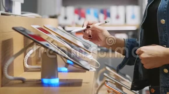 无法辨认的女人在电子商店里用手写笔尝试平板电脑视频的预览图