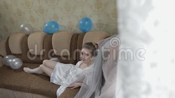 美丽可爱的新娘穿着睡衣和面纱躺在沙发上慢动作视频的预览图