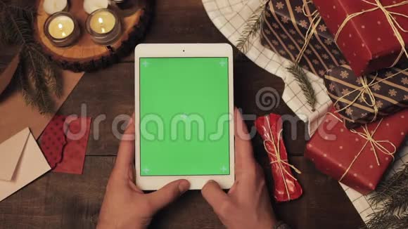 木制圣诞装饰桌上全新白色平板垂直绿色屏幕上的手贴顶视图视频的预览图