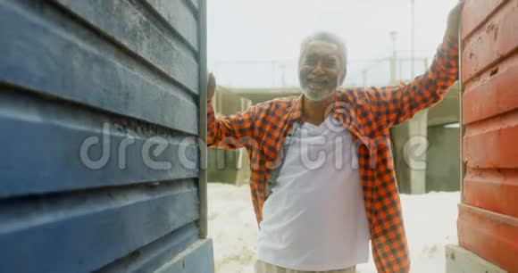 在阳光明媚的4k天气里站在海滩小屋的快乐活跃的非裔美国老人的正面景色视频的预览图