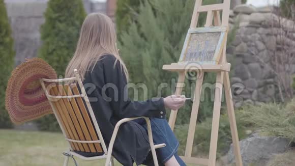 后景肖像的年轻女孩画家坐在木制画架前画一幅画和吸烟女性视频的预览图