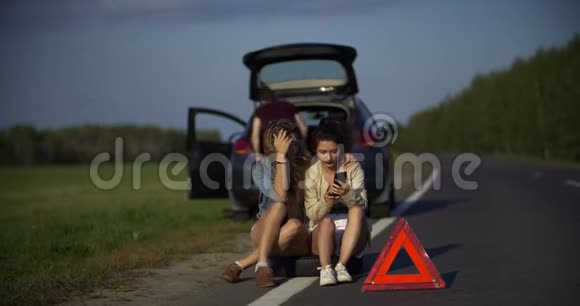 两个年轻的女人坐在电话里自拍而男人修理破车视频的预览图