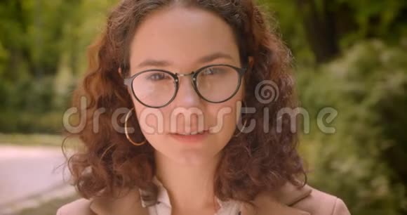 年轻漂亮的长发卷曲的高加索女性戴眼镜的特写照片微笑着愉快地看着镜头视频的预览图