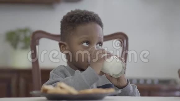 有趣的非洲裔美国儿童坐在桌子旁喝着杯子里的牛奶的肖像视频的预览图