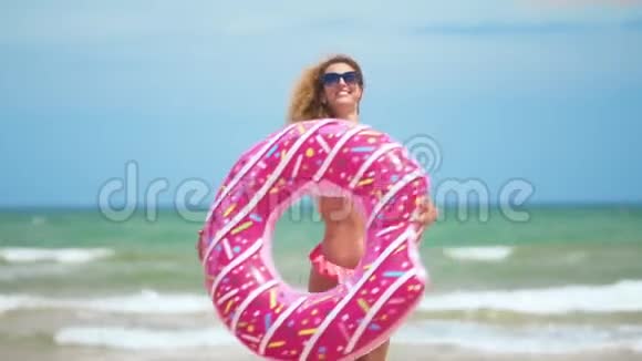 女人玩得开心笑着和粉红色的甜甜圈跳舞穿着比基尼的女孩在海滩上戴着太阳镜美丽性感的女人视频的预览图