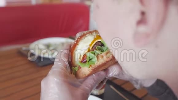 一个坐在咖啡馆里的男人正在吃一个开胃的大汉堡从后面看视频的预览图