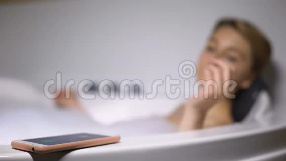 微笑的女人在浴缸里用泡沫泡泡打电话愉快的交谈视频的预览图
