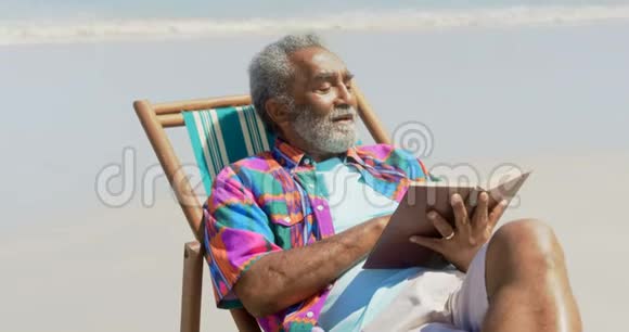活跃的非裔美国人在海滩4k的躺椅上看书的正面景色视频的预览图