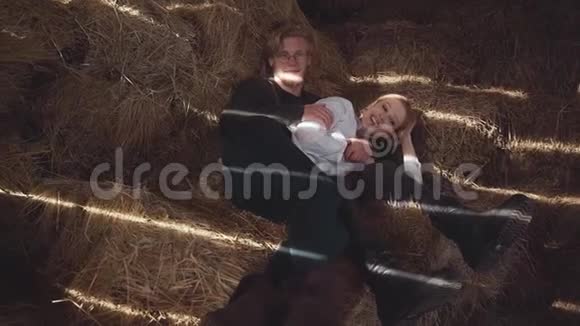 一对年轻夫妇躺在谷仓里拥抱干草快乐的微笑男孩和女孩花时间在一起慢动作视频的预览图