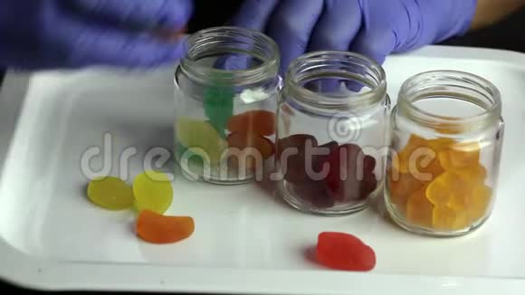 各种形状和颜色的果冻糖果散落在托盘上一个戴着橡胶手套的人把它们放进玻璃瓶里视频的预览图