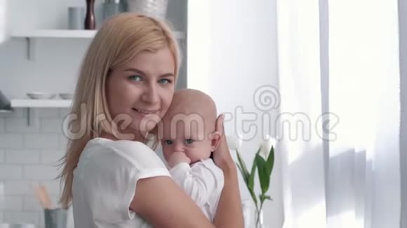 新妈妈拥抱亲吻厨房里的女婴家庭幸福的画像视频的预览图