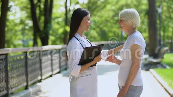 年轻护士在康复中心公园与老年妇女交谈视频的预览图