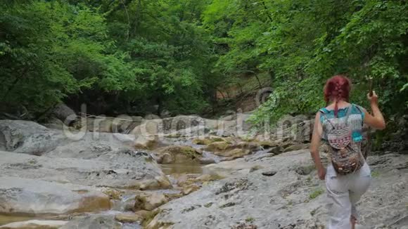 一个孤独的红发女孩沿着一条干净的山河沿着峡谷的底部行走视频的预览图
