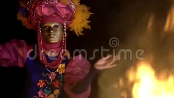 一个夜晚在火边神秘的舞蹈表演一个优雅的女孩穿着明亮的西装和金色的面具视频的预览图
