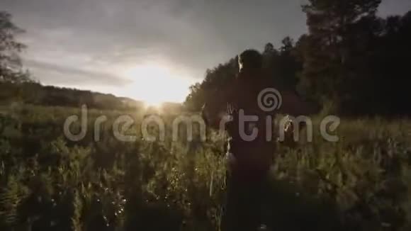 一个人带着长长的草跑过野绿色的田野的后景库存录像镜头跟随着美丽的奔跑者视频的预览图