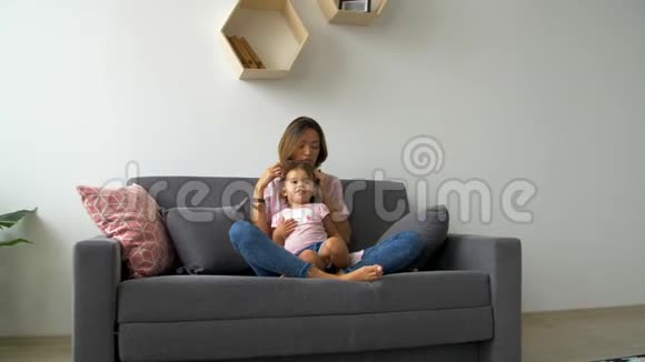 幸福美丽有爱的家庭年轻的母亲和女儿坐在沙发上笑着鬼鬼祟祟地走来走去视频的预览图