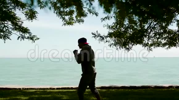 小剪影是一位年轻的运动员在湖岸积极从事体育运动交叉健身拳击跆拳道视频的预览图