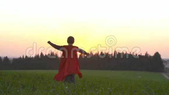 日落时穿着超级英雄斗篷的男孩在田野里奔跑视频的预览图