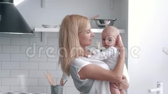 爱的母亲手牵着新生的女婴年轻女子的肖像轻轻拥抱和亲吻她的孩子在厨房视频的预览图