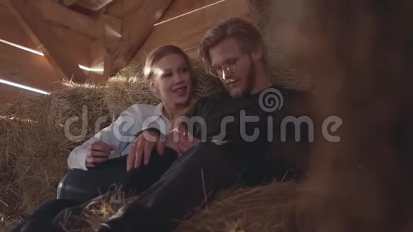 一对年轻漂亮的夫妇躺在寒冷的冬天谷仓的干草上的肖像年轻的农民每天工作后休息视频的预览图