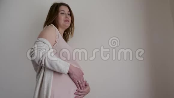 穿睡衣的孕妇站在房子的墙边中风视频的预览图