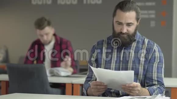 两位同事坐在办公室研究报纸上的新工作信息在后台问建议的年轻人视频的预览图
