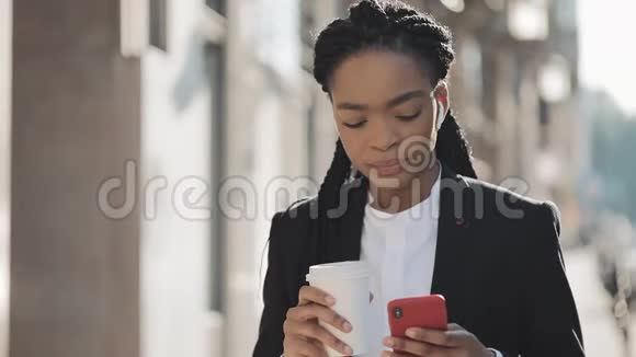 一位年轻的非洲裔美国女商人穿着西装站在老城背景上喝着咖啡和视频的预览图