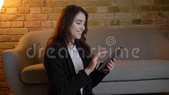年轻的白种人女孩留着波浪发坐在地板上看着平板电脑在舒适的家里展示着绿色的屏幕视频的预览图