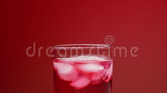 一个女人她的手搅动冰块在一杯冰和红色苏打水与气体红色背景慢速饮料概念视频的预览图