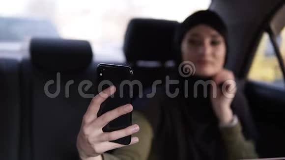 一位年轻迷人的穆斯林妇女戴着头巾在车上通勤的肖像她穿着深色衣服坐着视频的预览图